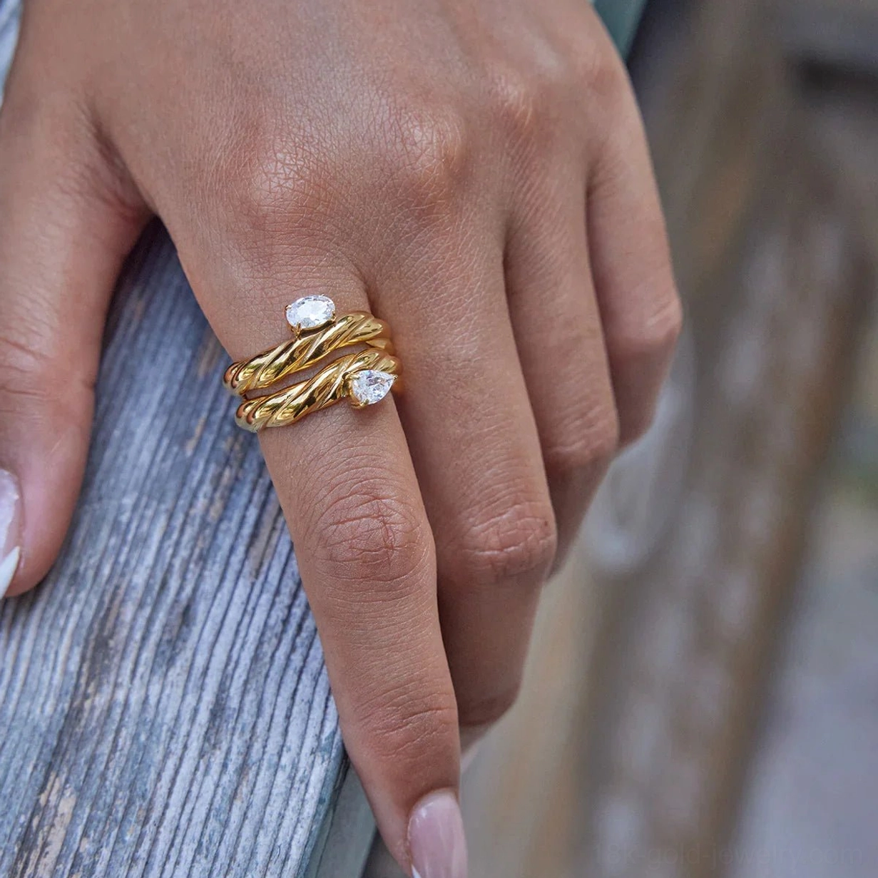 Double-stack 18K gold twisted rings with small gem accents on model's hand outdoor wooden backdrop