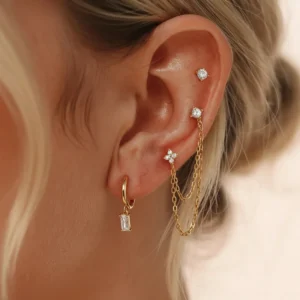 18K gold diamond drop hoops and chain studs layered on ear model, close-up side profile showing baguette CZ crystals and gold accents