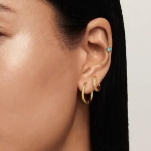 18K gold stackable earring set worn on female model, showcasing mix-and-match styling with blue stud, crystal pave hoop, and polished gold hoop layered together