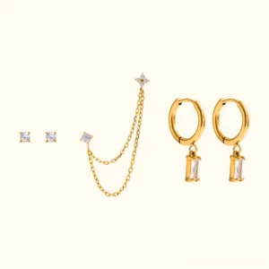 Complete 18K gold earring set flat lay featuring huggie hoops, delicate chain earring, and square crystal studs on beige background