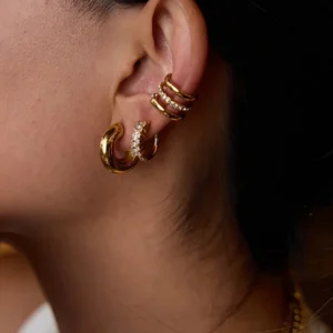 Gold earring trio rear view worn on ear showing stacked layered huggies cuff earrings and diamond-paved hoops from back
