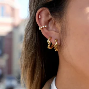 18k gold earring bundle styled on ear featuring wavy huggie hoops and crystal ear crawlers outdoors