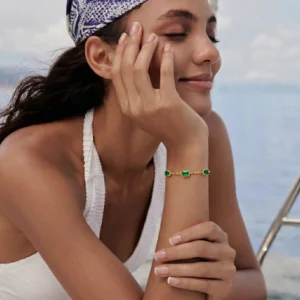 Woman wearing green emerald 18K gold station bracelet at seaside in casual halter top