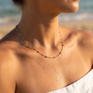 Delicate 18K gold necklace with colorful beads worn on model at seaside outdoor location