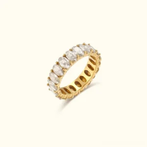 18K gold eternity ring with oval-cut diamond simulants in prong setting, flat lay view on beige background