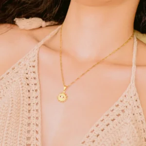 18K gold evil eye sun necklace worn on neck close-up showing delicate pendant resting at collarbone on female model in beige crochet top
