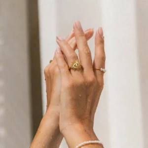 Evil eye gold ring worn on hand with matching jewelry, close-up detail shot showing radiating sunburst texture