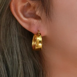18K gold textured hoop earrings worn on model's ear, close-up side view displaying engraved feather surface detail and polished finish