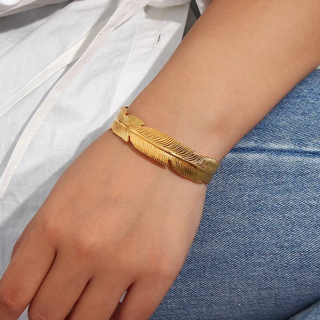 slim gold feather cuff bracelet on female wrist with white shirt and blue denim jeans casual style