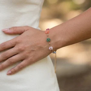 Floral gold bracelet on female wrist close-up, pastel flower accents with extendable gold chain clasp