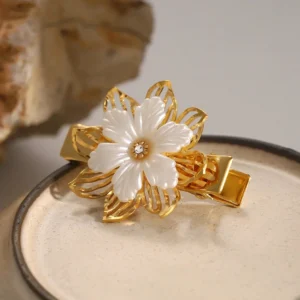 18K gold floral pearl hair clip three quarter side view - polished gold finish and layered flower design on ceramic display