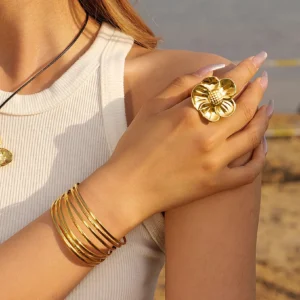 18K gold flower ring worn on hand stacked with thin gold bangles, close-up detail of textured petals, paired jewelry styling, female model
