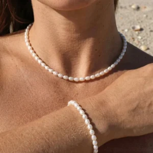Woman wearing freshwater pearl choker and bracelet set on beach sandy background close-up neck wrist detail