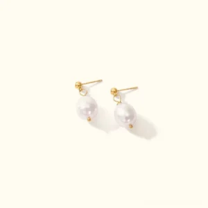 18K gold freshwater pearl drop earrings flat lay with baroque white pearls and gold hardware on beige background