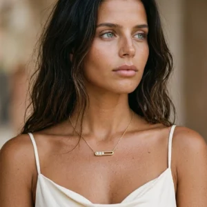 Minimalist 18K gold pendant necklace worn by woman with dark wavy hair, sitting at collarbone with delicate chain