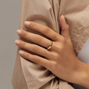 Geometric 18K gold band ring worn on female model hand with beige clothing close-up shot showcasing minimalist slim band design