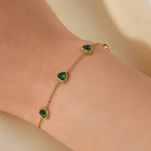 Waterproof 18K gold green heart bracelet worn on wrist close-up view showing heart-shaped gemstone charms and polished gold finish on skin