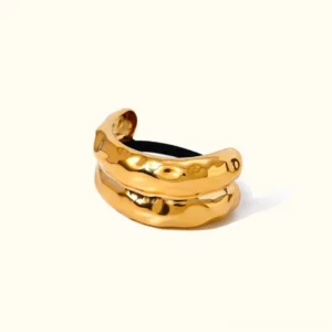 18K gold hammered arch hair cuff flat lay top-down view double-layer design black elastic base off-white background