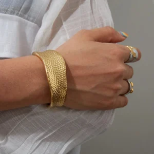 Hammered gold bracelet worn on wrist with linen shirt paired with stackable rings close-up
