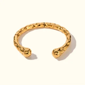 Hammered 18K gold open cuff bracelet flat lay overhead view with textured finish on neutral background