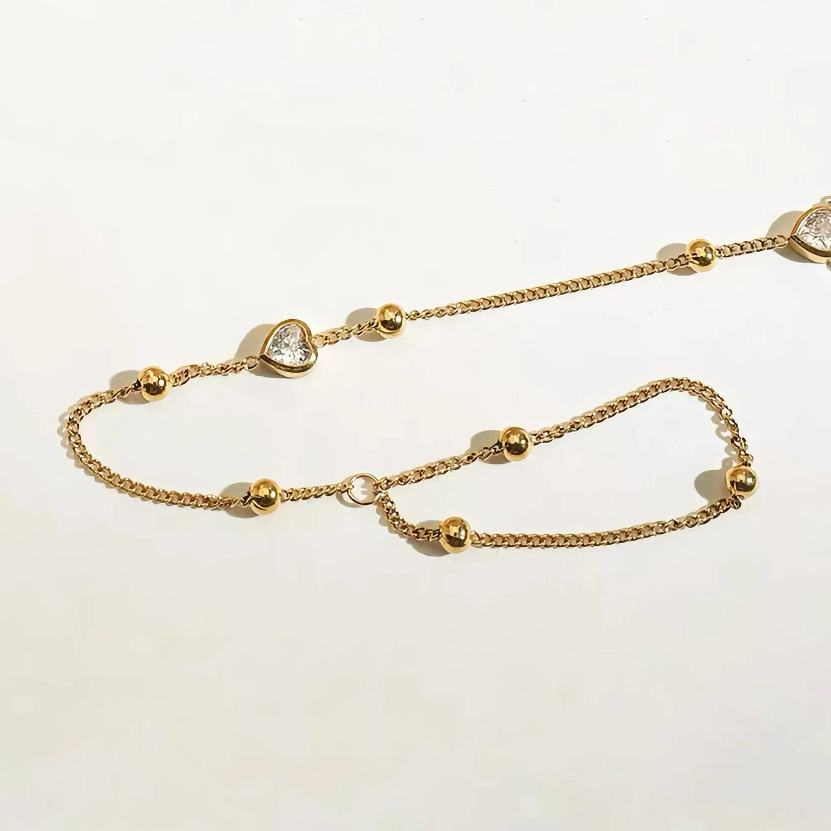 Dual 18K gold hand chains with bead accents and cubic zirconia heart charms, flat lay comparison view on light background