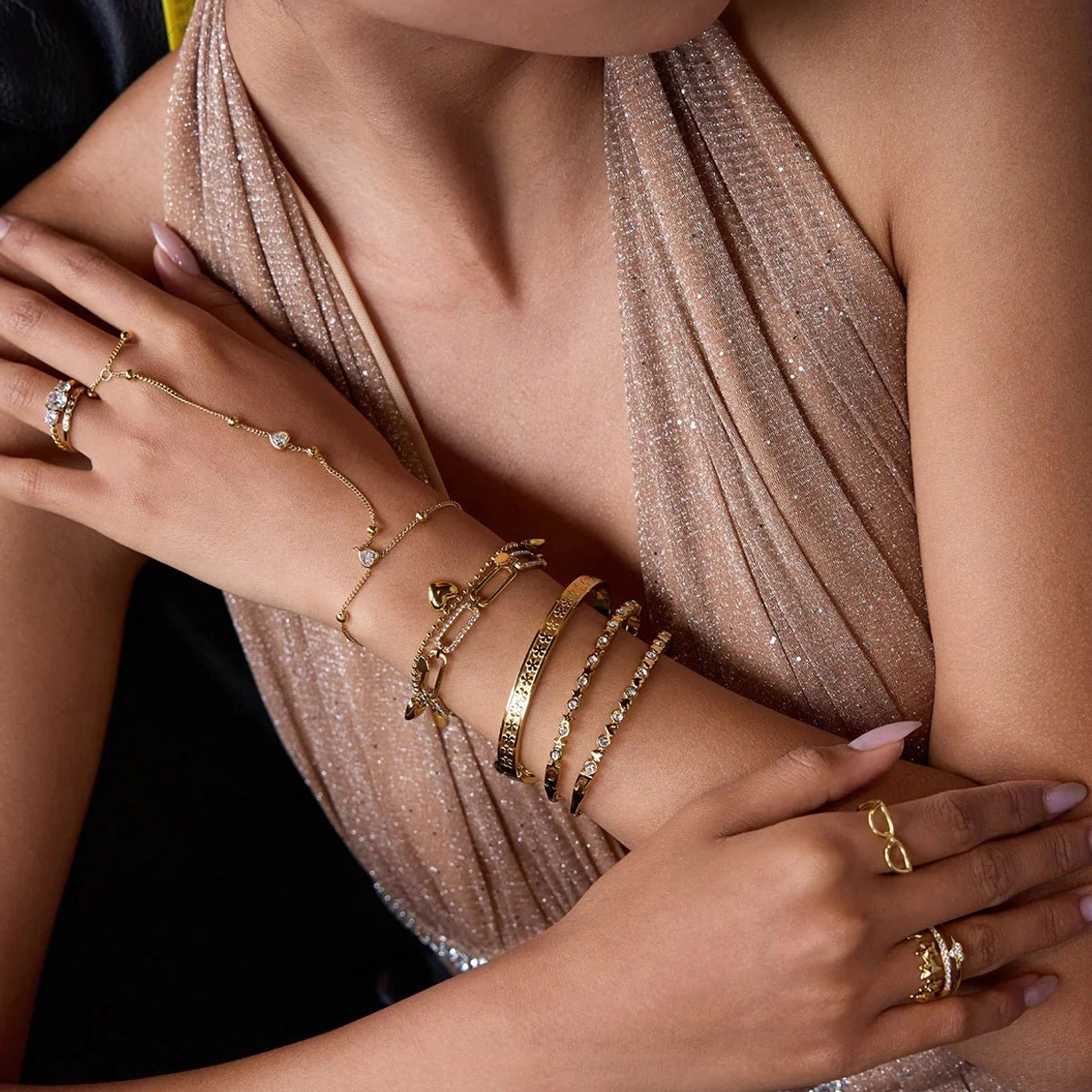 18K gold hand chain bracelet stacked with matching rings and bracelets on elegant female model wearing champagne halter gown