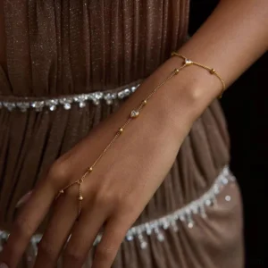 Delicate 18K gold hand chain worn on female model, thin gold finger chain with heart-shaped charm, close-up side view styling