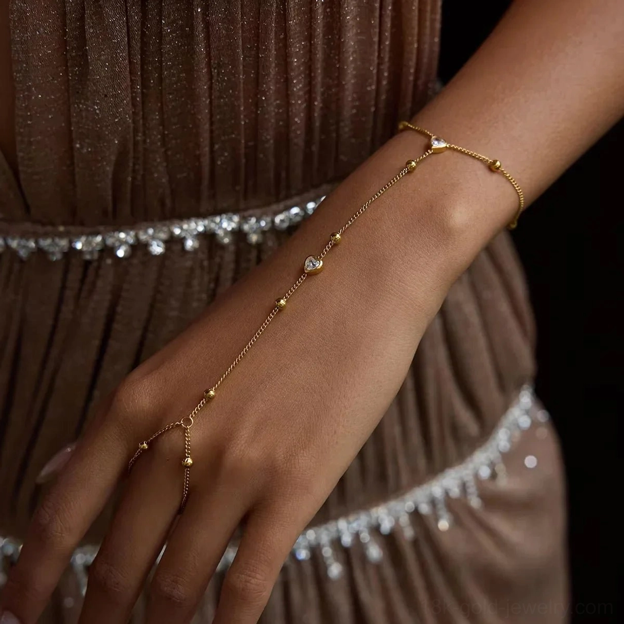 Delicate 18K gold hand chain worn on female model, thin gold finger chain with heart-shaped charm, close-up side view styling