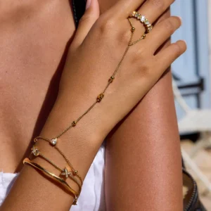 18K gold hand jewelry stack bundle worn by model - four-piece layered set featuring gold hand chain, diamond ring, herringbone bracelet and gold bangle on hand in outdoor casual setting