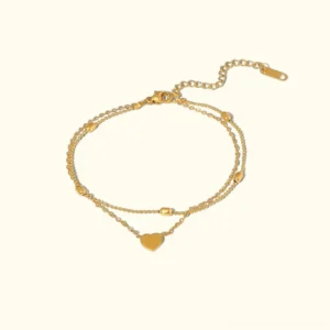 18K gold layered heart anklet flat lay overhead shot showing double-chain design with heart charm and bead accents on light background