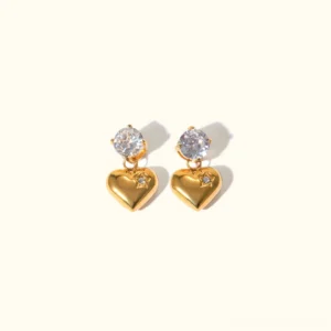 18K gold heart drop earrings with cubic zirconia studs, top-down flat lay view on neutral beige background, polished gold finish showing detailed heart charm design