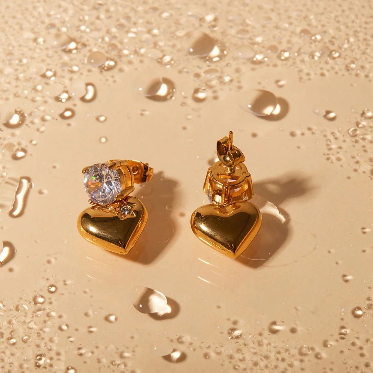 18K gold heart drop earrings on wet terracotta surface, water-resistant demonstration flat lay, showing polished texture and durable cubic zirconia stones
