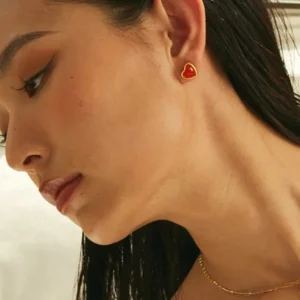 Woman wearing 18K gold heart stud earrings on left earlobe close-up side profile with soft indoor lighting