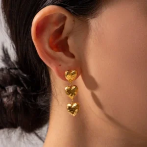 Close-up side view of 18K gold heart dangle earrings worn on ear showcasing textured design