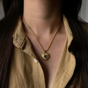 Gold heart necklace worn on model at collarbone level, vintage finish with green gemstone center