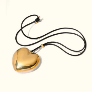 18K gold heart pendant necklace with polished finish and black wax cord flat lay view on plain background