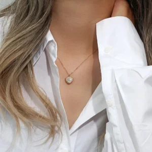 Woman wearing delicate 18K gold heart pearl necklace on collarbone, white button-up shirt, close-up neck jewelry styling photo