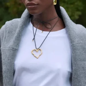 Layered 18K gold heart pendant necklaces worn by model, upper body close-up outdoors with green foliage, casual styling demonstration