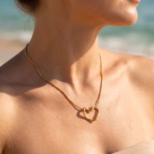 Gold heart knot pendant necklace worn on bare shoulder woman beach outdoor close-up