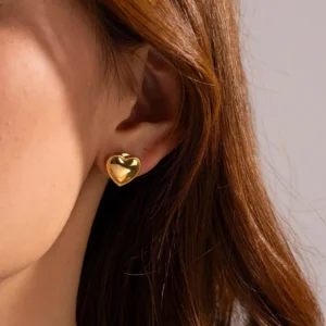 18K gold heart stud earrings worn on ear, close-up detail of woman wearing single gold heart earring on earlobe