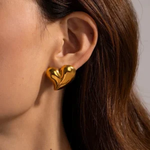 Gold heart earrings on ear close-up side view worn by model elegant jewelry