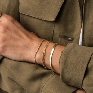 Layered stackable 18K gold herringbone bracelet worn on wrist with brown jacket styling inspiration