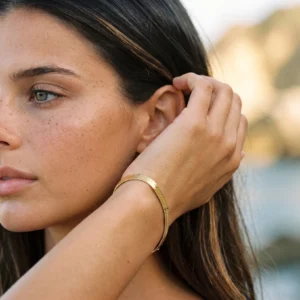 Slim gold herringbone bracelet worn on left wrist with polished texture detail shot
