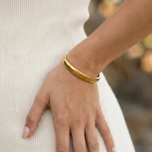 Close-up side view of gold bangle bracelet fitted on wrist with smooth shiny finish against cream fabric background