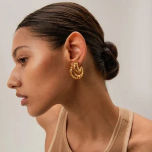 Gold hollow hoop earrings worn on model's earlobe side profile view displaying carved texture and shiny finish