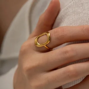 Close-up side view of 18K gold hollow oval ring worn on female hand with fabric, showing smooth gold surface and oval frame design