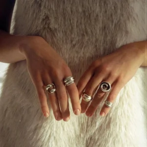 Close-up hand model wearing 18K gold twisted coil statement rings and chunky hollow band jewelry pieces