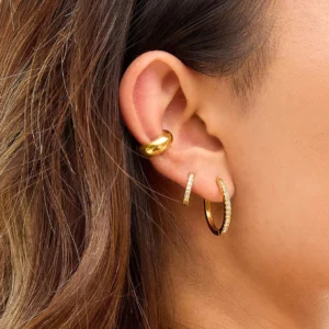 18K gold hoop earrings layered on ear - slender diamond hoops and chunky gold hoop worn together, showing contemporary stacking style on light brown hair model