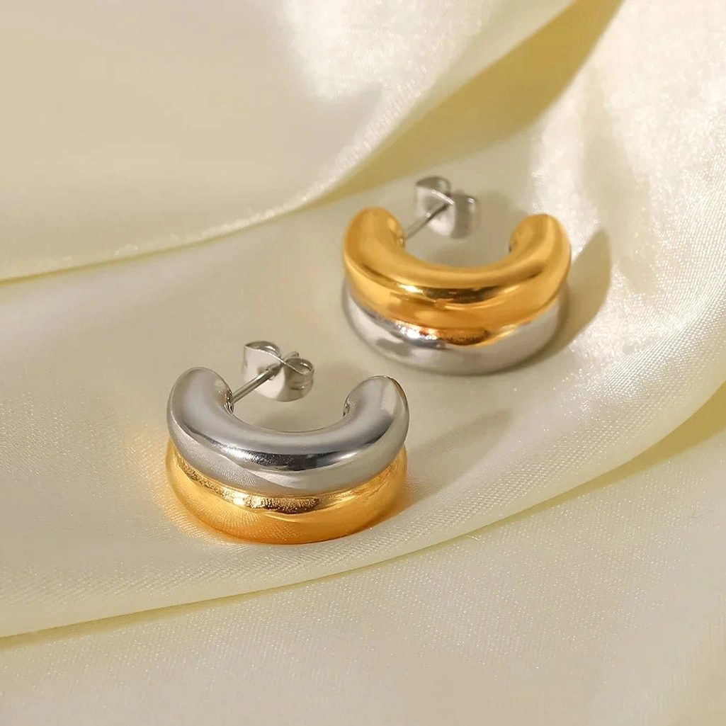 Multiple pairs of 18K gold and two-tone hoop earrings displayed on ivory satin, showing both styles together