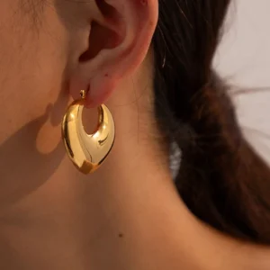 18K gold hoop earrings worn on ear, close-up side view showing hinged clasp and shiny reflective gold surface